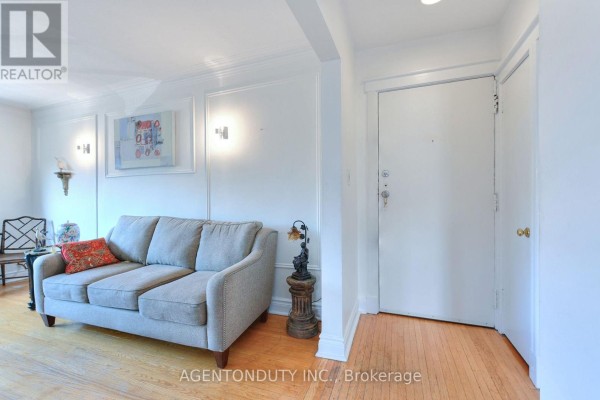 Living room with a grey sofa, light wood floor, and a white door. - 17 - 1646 Bathurst Street, Toronto