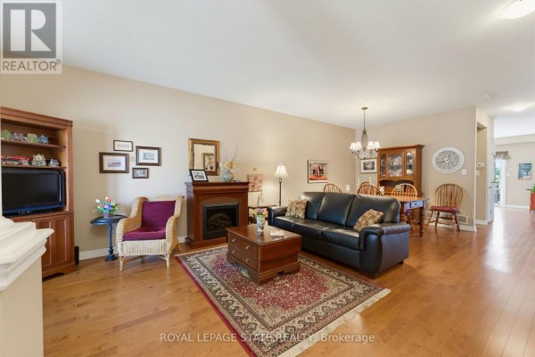 Living room with hardwood floors, a fireplace, black leather sofa, and dining area with a wooden table. - 17 - 310 Southbrook Drive, Hamilton