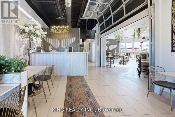 Spacious restaurant interior with greenery, tables, and large windows overlooking the patio. - 17 - 3175 Rutherford Road, Vaughan
