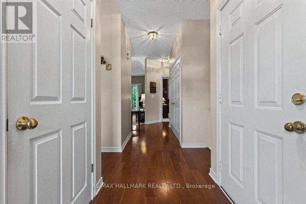 View down a long interior hallway with hardwood floors and multiple doors. - 17 - 99 Linwell Road, St  Catharines
