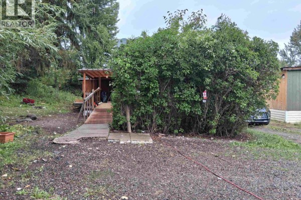 Side view of the mobile home with an overgrown bush and wooden ramp. - 17 2123 Riverside Drive, Smithers
