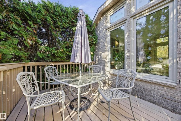 A wooden deck with a glass table, chairs, and umbrella. - #17 26417 Twp Road 512, Rural Parkland County