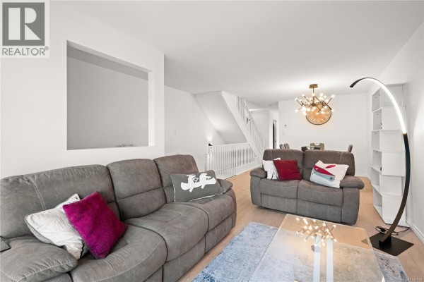 Living room with grey sofas, a glass coffee table, and a view of the dining area and staircase. - 17 478 Culduthel Rd, Saanich