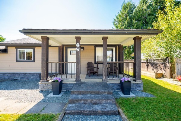 Front porch of a beige house with wooden pillars, railings, and two Adirondack chairs. - 17 8985 Shook Road, Mission