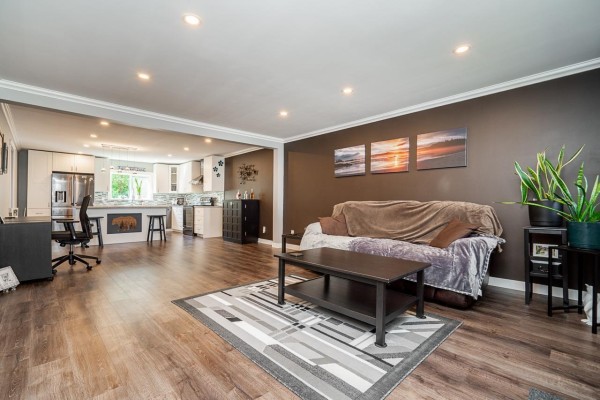 Living room with a brown sofa, coffee table, and an open-concept view to the white kitchen. - 17 8985 Shook Road, Mission
