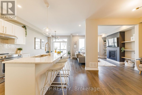 Open concept living area with a white kitchen island, dining table, and living room with fireplace. - 17 Allan Moore Place, Ottawa
