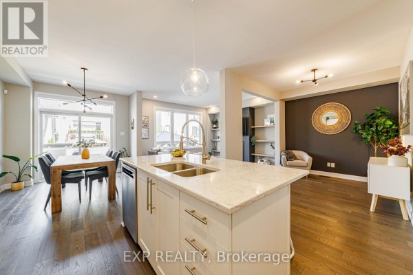 Kitchen island with sink, dining area with dark wood table and chairs, and living room beyond. - 17 Allan Moore Place, Ottawa