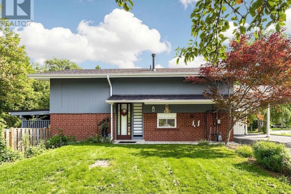 Front of the house with red brick lower level and blue siding upper level, featuring a green lawn and trees. - 17 Amboy Road, Toronto