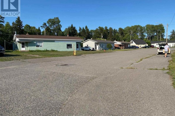 A street view of single-story houses with green lawns and paved driveways under a clear blue sky. - 17 Birch Crescent, Terrace Bay