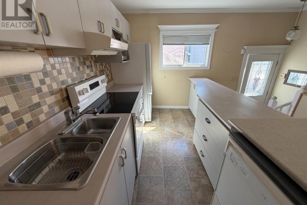 Close-up of a kitchen sink and faucet with white cabinets and a beige countertop, featuring a patterned backsplash. - 17 Brown Rd, Elliot Lake