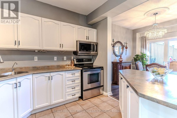 White kitchen with stainless steel appliances, laminate countertops, and view of dining area. - 17 Bruce Crescent, Barrie