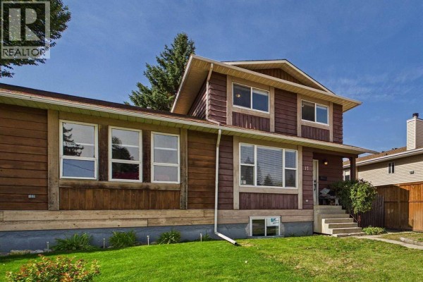 Side exterior view of a duplex with brown wood siding and a large front window. - 17 Deermeade Road Se, Calgary