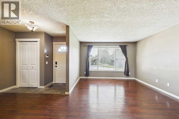 Living room with dark hardwood floors, light grey walls, and a large picture window. - 17 Deermeade Road Se, Calgary