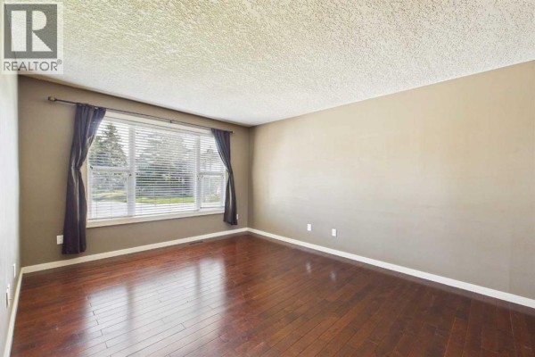 Interior view of an empty living room with dark hardwood floors and neutral walls. - 17 Deermeade Road Se, Calgary