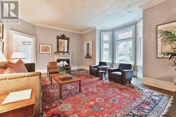 Living room with fireplace, leather armchairs, large red rug, and bay windows with natural light. - 17 Elm Avenue, Toronto