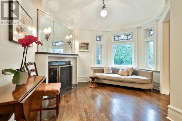 Sitting area with built-in curved sofa, fireplace with marble surround, and bay windows with stained glass. - 17 Elm Avenue, Toronto
