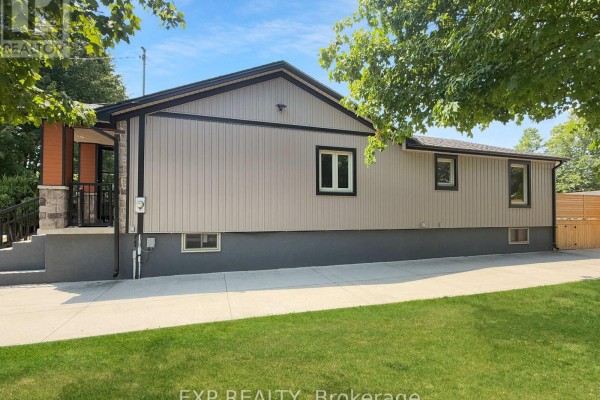 Side view of the house showing beige vinyl siding, dark trim, and a concrete foundation. - 17 Greenfield Court, London South