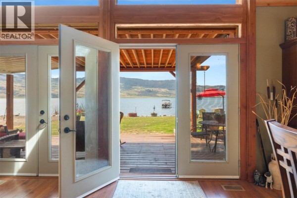 View from inside a house looking out double glass doors to a lake and outdoor seating. - 17 Mary's Emerald Bay Road, Vernon