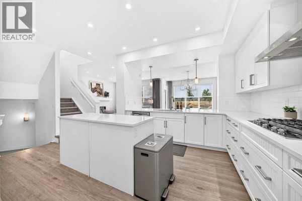 White kitchen with a central island, white cabinets, and light wood floors, showing a staircase. - 17 Masters Terrace Se, Calgary