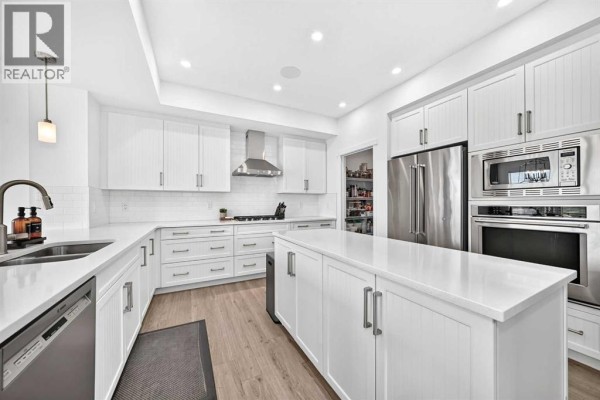 Spacious white kitchen featuring a large island, stainless steel appliances, pantry, and staircase. - 17 Masters Terrace Se, Calgary