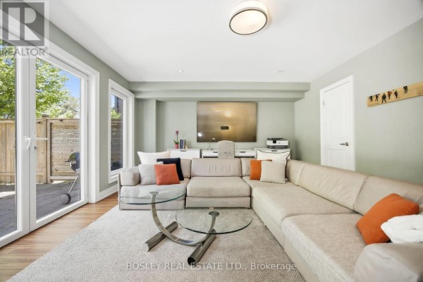 A sectional sofa, glass coffee table, and large windows overlook a backyard patio. - 17 Matthew Court, Toronto