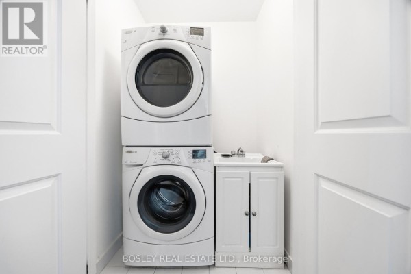A white stacked washer and dryer with a utility sink in a bright laundry room. - 17 Matthew Court, Toronto