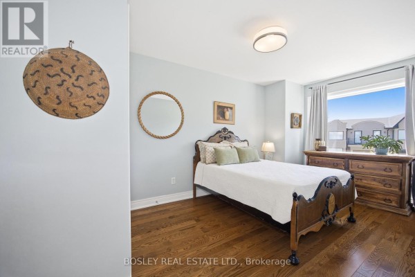 A bedroom with hardwood floors, a bed, dresser, and a large window overlooking townhouses. - 17 Matthew Court, Toronto