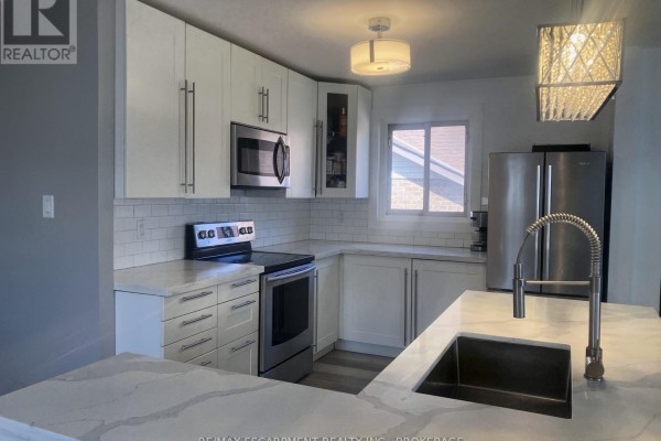 Corner view of a white kitchen featuring stainless steel appliances, subway tile, and marble countertops. - 17 Mellenby Street, Hamilton