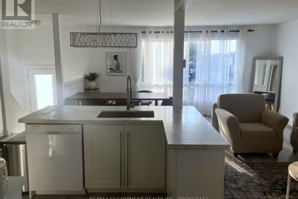 Open-concept living area with a kitchen island, dining table, chairs, and natural light from patio doors. - 17 Mellenby Street, Hamilton