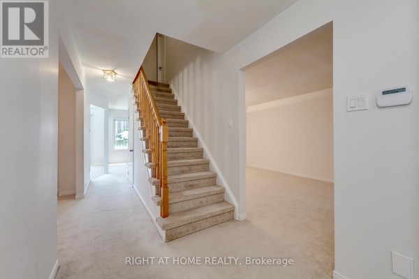 Interior view of a hallway with a carpeted staircase, light beige walls, and doorway. - 17 Nickel Crescent, Brampton