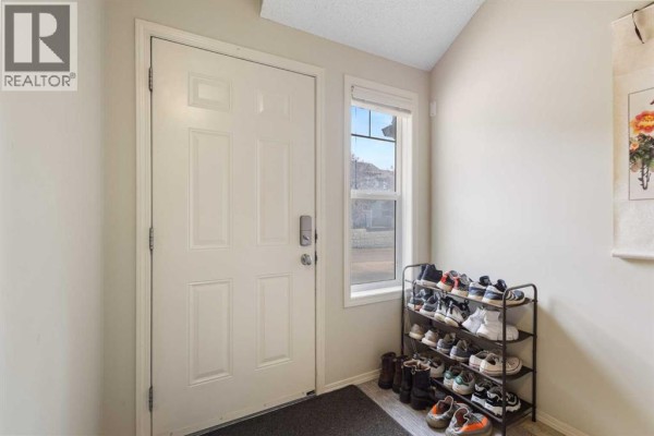 Entrance foyer with white door, window, and shoe rack holding multiple pairs of shoes. - 17 Panatella Villas Nw, Calgary