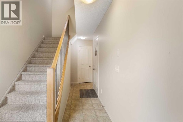 Interior hallway and staircase with beige carpeted stairs and tiled floor. - 17 Panatella Villas Nw, Calgary