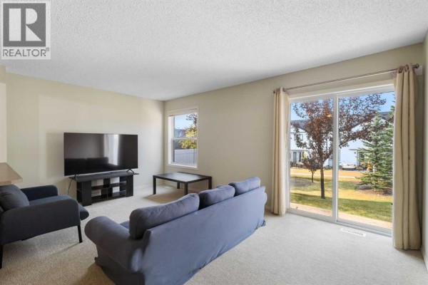 Living room with blue sofa, armchair, television, and sliding glass doors to backyard. - 17 Panatella Villas Nw, Calgary