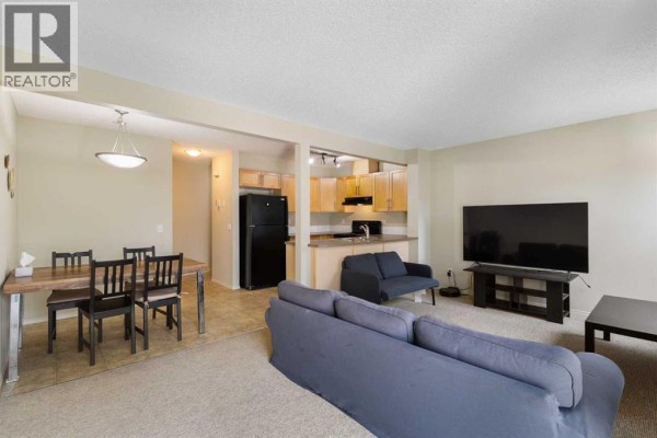 Open concept living, dining, and kitchen area with wooden table and beige carpet. - 17 Panatella Villas Nw, Calgary