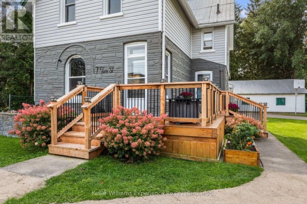 Front view of a two-story house with gray stone and white siding, featuring a wooden deck and a pathway. - 17 Stone Street, Springwater