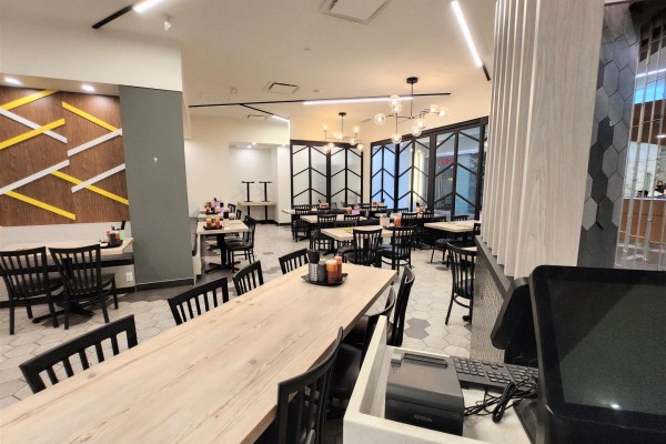 Restaurant seating area with long wooden tables, black chairs, and modern lighting. - 170, 10235 101 Street Nw, Edmonton