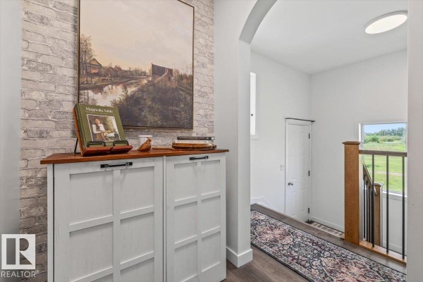 Hallway with white storage cabinets against a textured brick wall and a wooden shelf with decor. - #170 22169 Twp Road 530, Rural Strathcona County