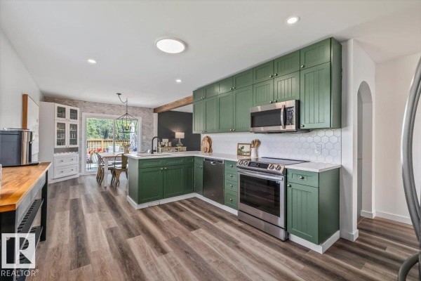 Green kitchen cabinets with stainless steel appliances and white hexagonal tile backsplash, connected to dining area. - #170 22169 Twp Road 530, Rural Strathcona County