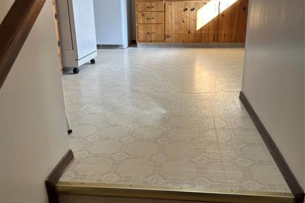 View of a light-colored linoleum floor with a patterned design and wood trim leading towards a kitchen. - 170 7th Avenue Sw, Minnedosa