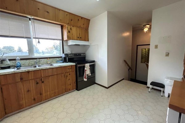 Kitchen area featuring a double sink, stainless steel stove, wood cabinets, and a view of the backyard through the window. - 170 7th Avenue Sw, Minnedosa