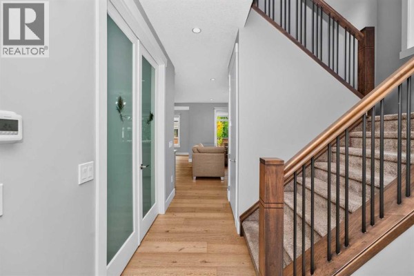 Hallway with frosted glass doors, hardwood floors, and a carpeted staircase with wood railing. - 170 Kinniburgh Crescent, Chestermere
