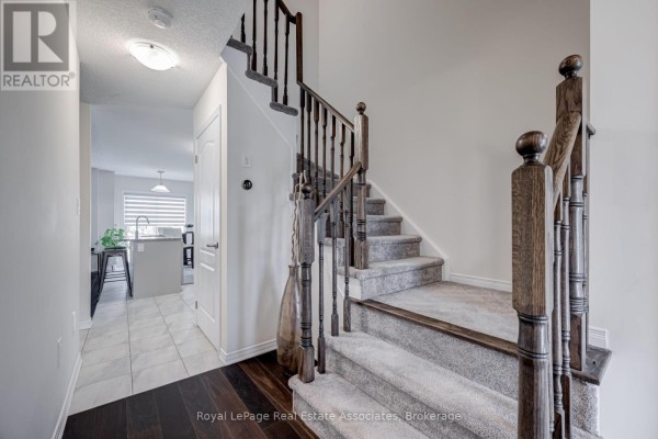 Interior staircase with dark wood banister and new carpet, leading towards a kitchen area. - 170 Maclachlan Avenue, Haldimand