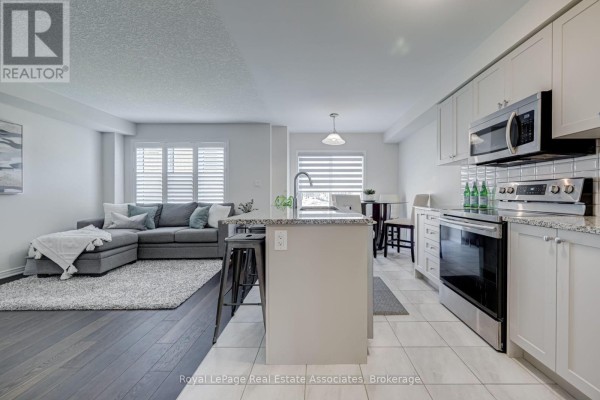 Open concept living area and kitchen with a grey sectional sofa, island, and white cabinets. - 170 Maclachlan Avenue, Haldimand
