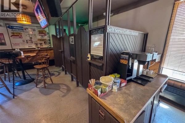 Dining area with tables and chairs, a bar in the background, and patterned flooring. - 170 Main Street, Bengough