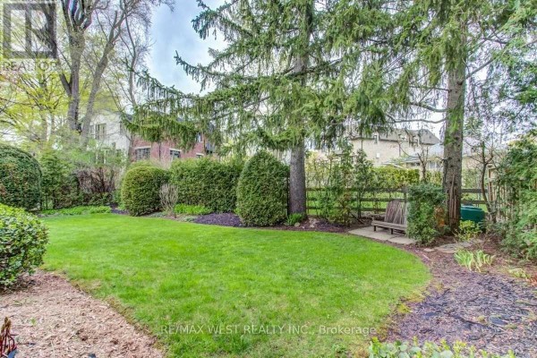 Backyard with green lawn, hedges, trees, and a wooden bench - 170 Newton Drive Toronto