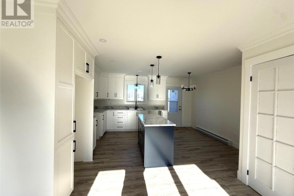 Kitchen with white cabinetry, a dark blue island, and pendant lights above the island. - 170 Penwell Avenue, Gander