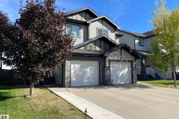 Side view of a duplex showing the front facade with a double garage and paved driveway. - 17005 120 St Nw, Edmonton