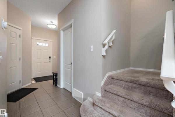 Entryway with tiled floor, staircase with carpeted steps, and a view of the front door. - 17005 120 St Nw, Edmonton