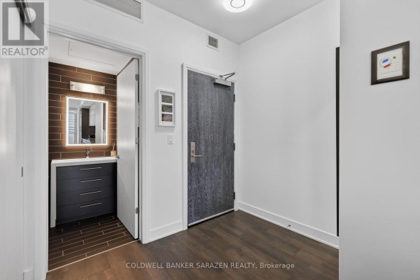 Interior entryway with a dark wood door, modern vanity, and dark tiled bathroom. - 1702 - 428 Sparks Street, Ottawa