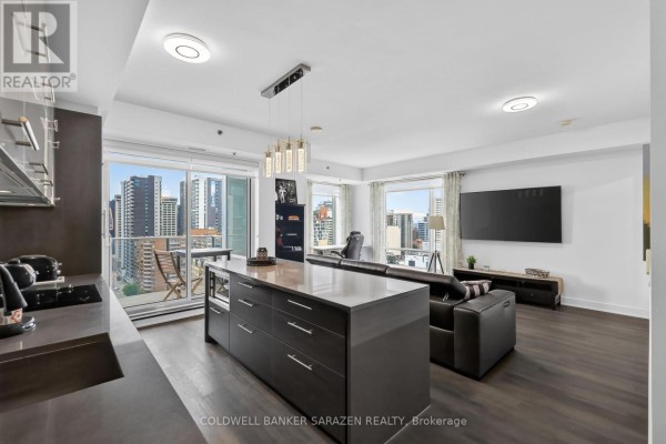 Open concept living area with a kitchen island, sofa, and city views from windows. - 1702 - 428 Sparks Street, Ottawa